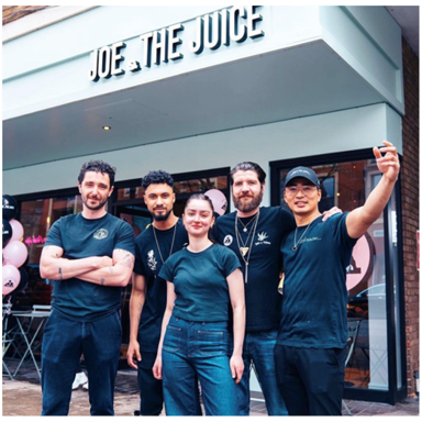 Eine Gruppe von Arbeitnehmern der Kette "Joe and the Juice" steht im Eingangsbereich des Lokals und lächelt in die Kamera.