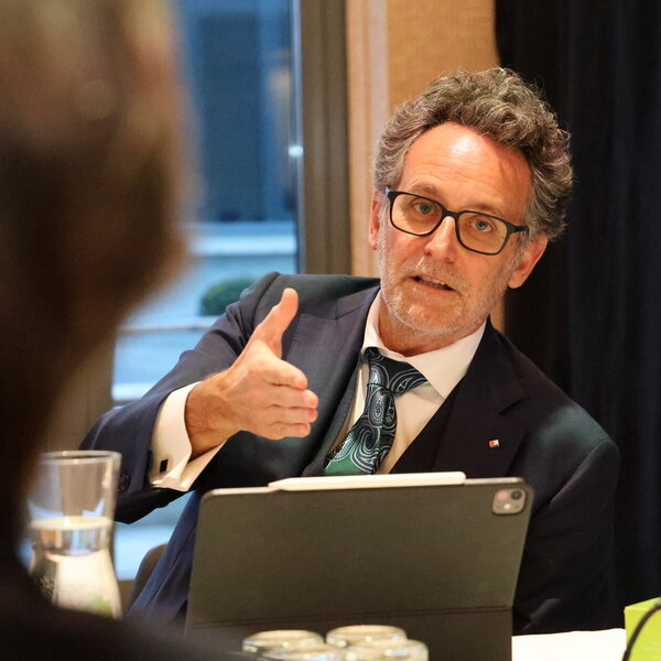 Ein Geschäftsmann mit Kravatte sitzt an einem Tisch spricht mit seinem Gegenüber.