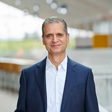 Portraitfoto von Rüdiger Kasch, Geschäftsführer von Alnatura; Mann gekleidet in weißem Hemd und blauem Sakko, im Hintergrund ist ein Firmengelände leicht verschwommeb erkennbar