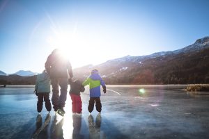 Familie fährt Schlittschuh auf einem zugefrorenen See in den Bergen